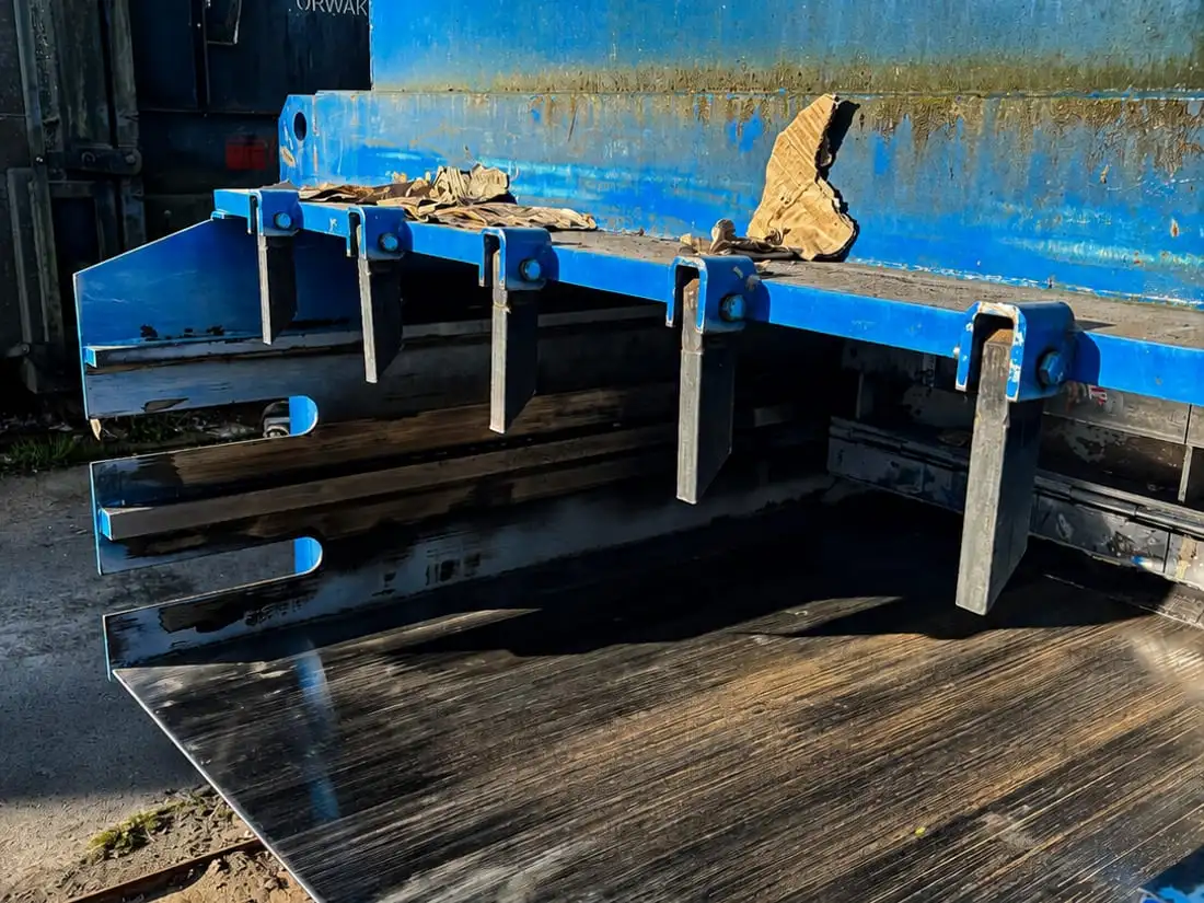 Rad av nymonterade ståltänder längs överkanten i ett blått flak, med en ny blank bottenplåt under.