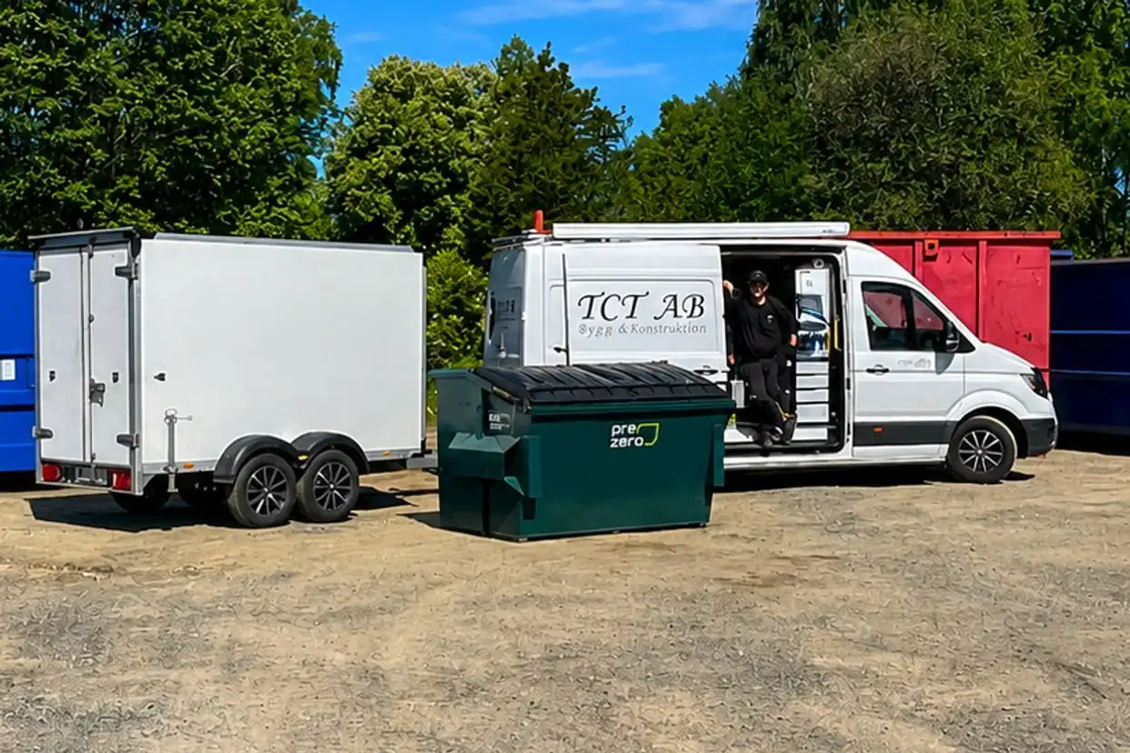 TCT:s vita servicebil med öppen sidodörr och en täckt släpvagn på grusgården i Tenhult, med containrar och ett avfallskärl omkring.